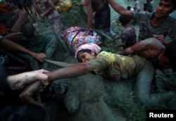 Photographers help a Rohingya refugee come out of Nad River as they cross the Myanmar-Bangladesh border in Palong Khali, near Cox's Bazar, Bangladesh, Nov. 1, 2017.