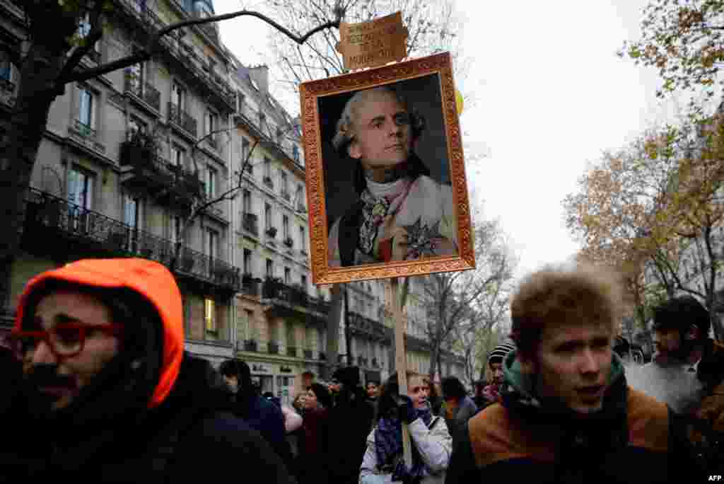 A woman holds a portrait of French President Emmanuel Macron painted as a royalty with a sign on top of it reading "14 mai 2017 restoration of the monarchy" during a demonstration against the pension overhauls, in Paris.