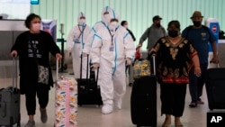FILE - Flight crew members in hazmat suits and passengers walk through the arrivals area at Los Angeles International Airport, in Los Angeles, California, Nov. 30, 2021.