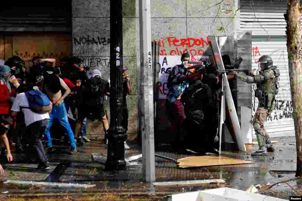 A police officer points his gun at the demonstrators during a protest against Chile's state economic model in Santiago, Oct. 22, 2019.