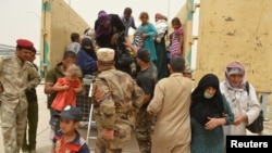 FILE - Iraqi soldiers help civilians, who fled from Falluja because of Islamic State violence, during a dust storm on the outskirts of Fallujah, Iraq, June 18, 2016