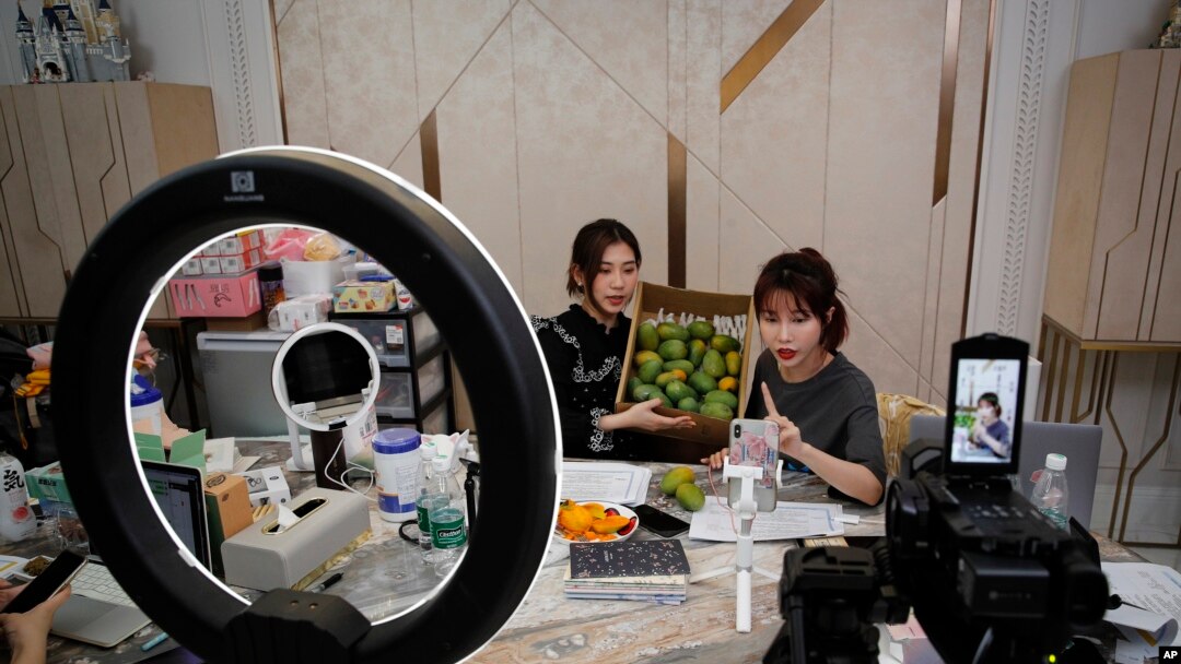 In this May 5, 2020, photo, China's online celebrity Zhang Mofan, right, introduces fresh mangos to her online clients and fans through the live-streaming at her house in Beijing.