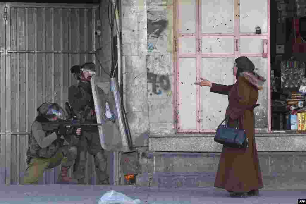A woman gestures at Israeli security forces firing rubber-bullets to disperse Palestinian stone-throwers amid clashes in the West Bank town of Hebron, Feb. 9, 2022. Israeli forces killed three Palestinians on Feb. 8 during a daytime raid against what Israel described as a "terrorist cell", leaving a vehicle in the West Bank city of Nablus riddled with bullet holes. 