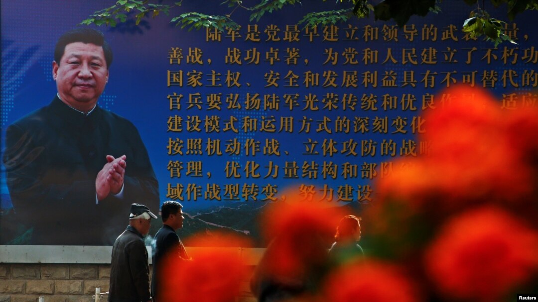 Men walk past a poster of the Chinese People's Liberation Army (PLA) featuring a portrait of President Xi Jinping, on the second day of plenary sessions of the 18th Central Committee of the Communist Party of China (CPC) in Beijing, Oct. 25, 2016.