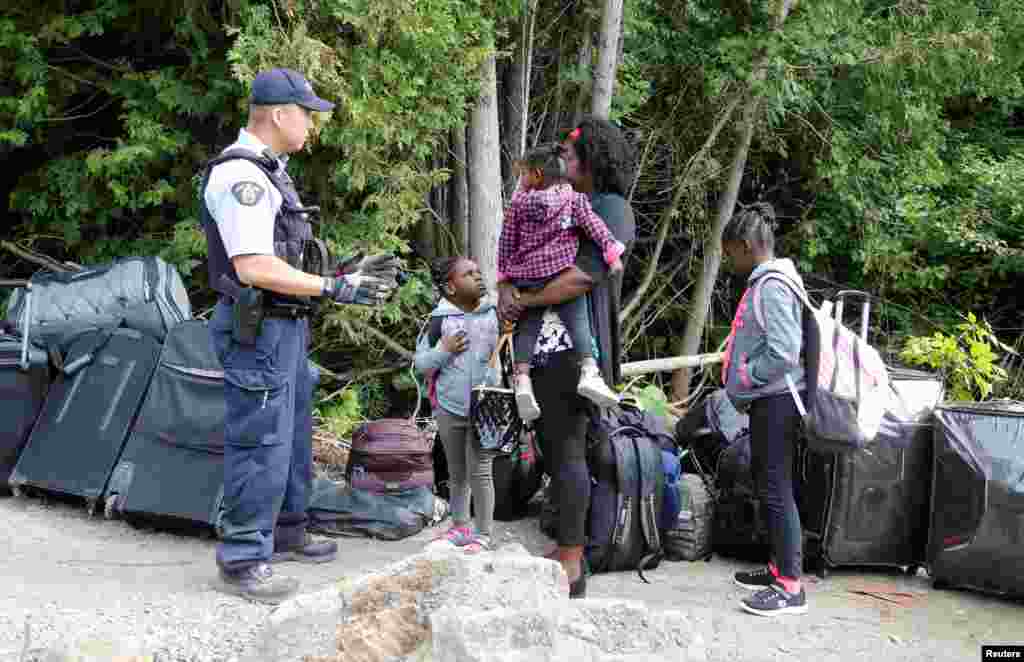 A family who identified themselves as from Haiti are confronted by a Royal Canadian Mounted Police officer as they try to enter into Canada from Roxham Road in Champlain, New York, Aug. 7, 2017.