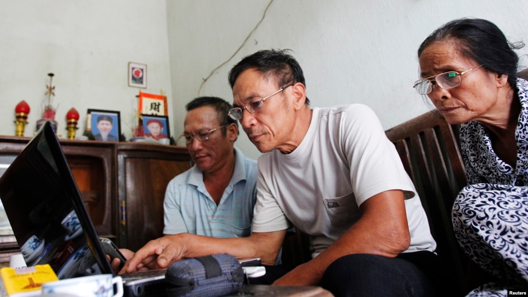 FILE - Veteran Le Dung (C) reads articles on the Internet with Dang Van Dat (L) and Tran Thi Thanh Kiem (R) at his house in Van Giang district, outside Hanoi, Vietnam.