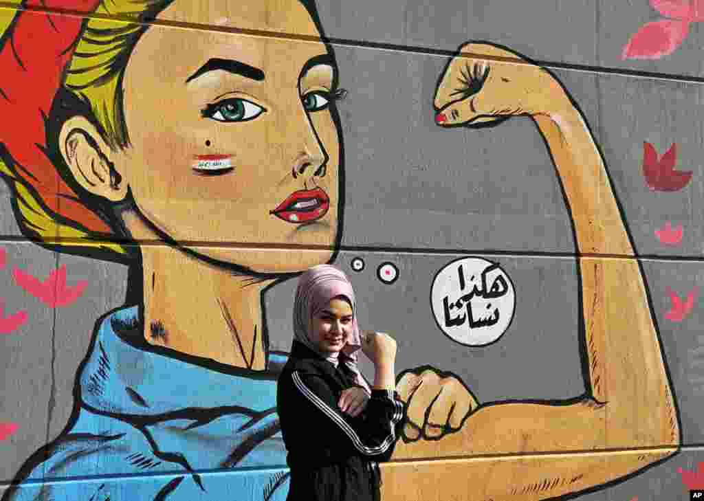 A woman poses for a picture in front of a graffiti with Arabic reading "those are our women" during ongoing protests near Tahrir Square in Baghdad, Iraq.