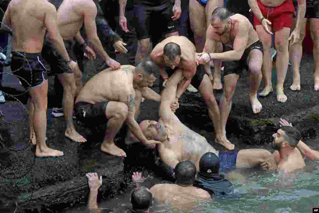 Swimmers pull a Greek Orthodox faithful who lost consciousness, out of the water as he swam with others to retrieve a wooden crucifix during the Epiphany ceremony in Istanbul, Turkey.