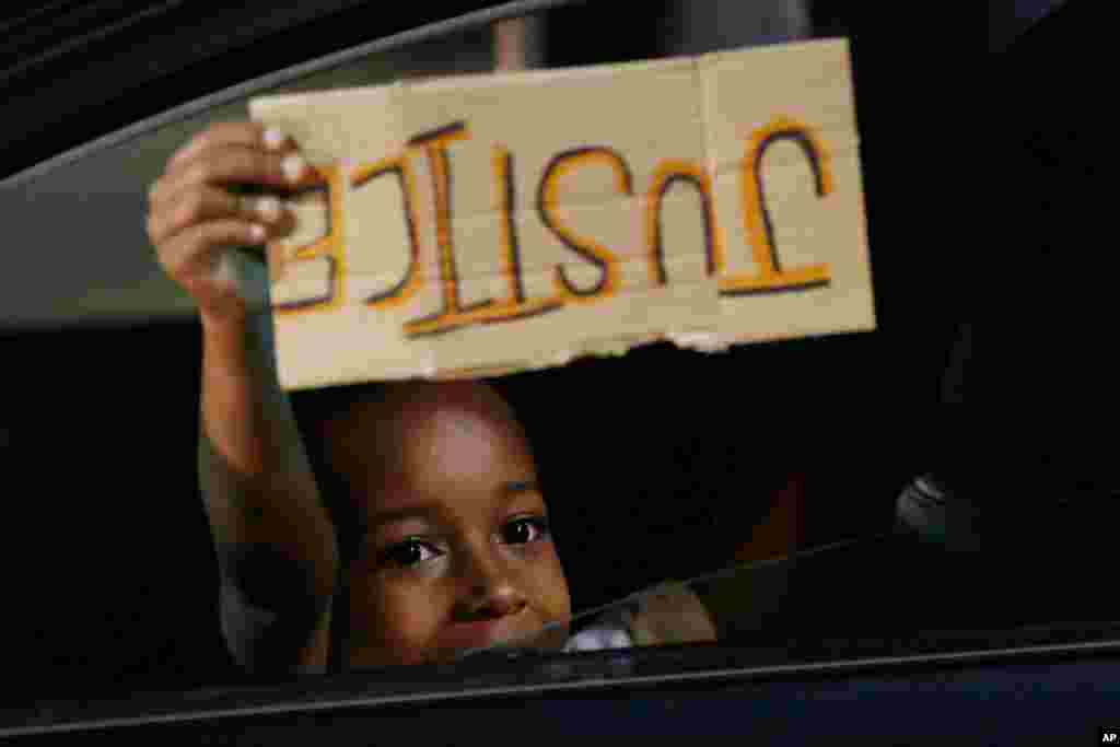 A young boy holds a "Justice" sign as he peers outside the window of a car passing protesters marching through downtown for a third night of unrest Sunday May 31, 2020, in Richmond, Va.