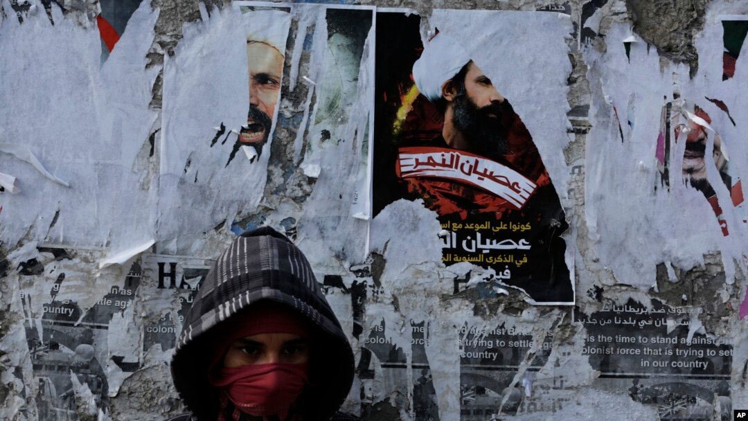 FILE - A Bahraini anti-government protester watches for riot police from in front of a wall with posters of a Shiite cleric executed in Saudi Arabia and other opposition posters that have been torn by authorities in Sitra.