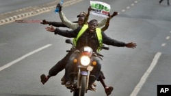 FILE - A motorcycle carrying protesters holding a placard using the acronym of the national electoral commission, drives ahead of demonstrators on foot calling for the disbandment of the commission over allegations of bias and corruption, in Nairobi, Kenya, June 6, 2016.