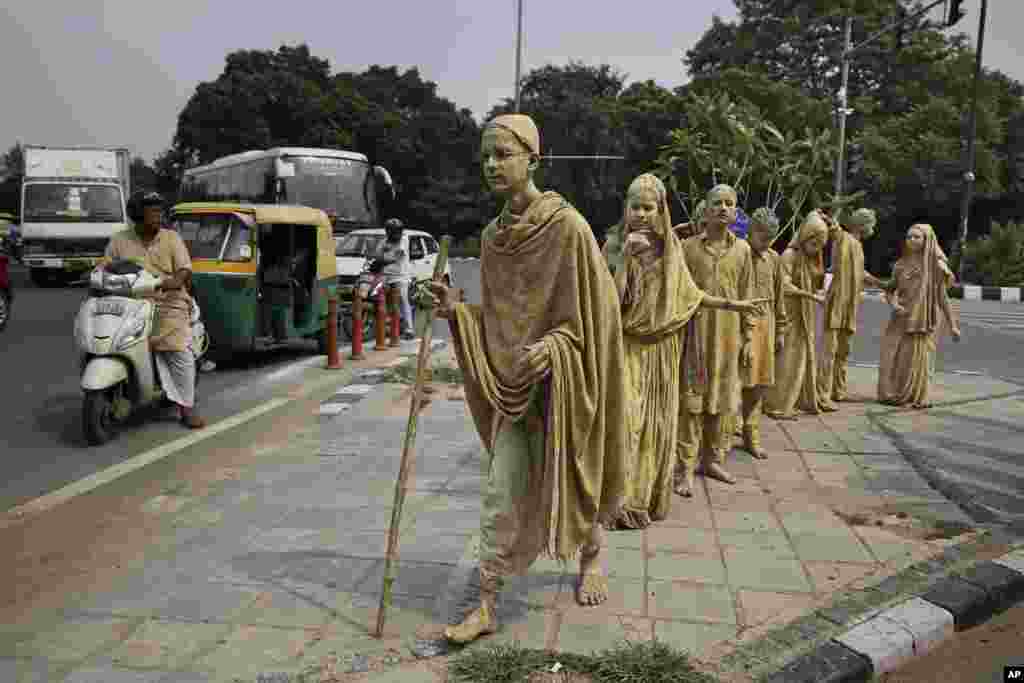 School children dressed up as statues, depicting Indian freedom leader Mahatma Gandhi's Dandi March, stand at a traffic intersection on the eve of Gandhi's 150th birth anniversary in New Delhi.