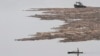 FILE - A North Korean man rows a boat past logs, which were tied together and transported by boats on the Yalu River near the North Korean city of Hyesan, Aug. 16, 2014.