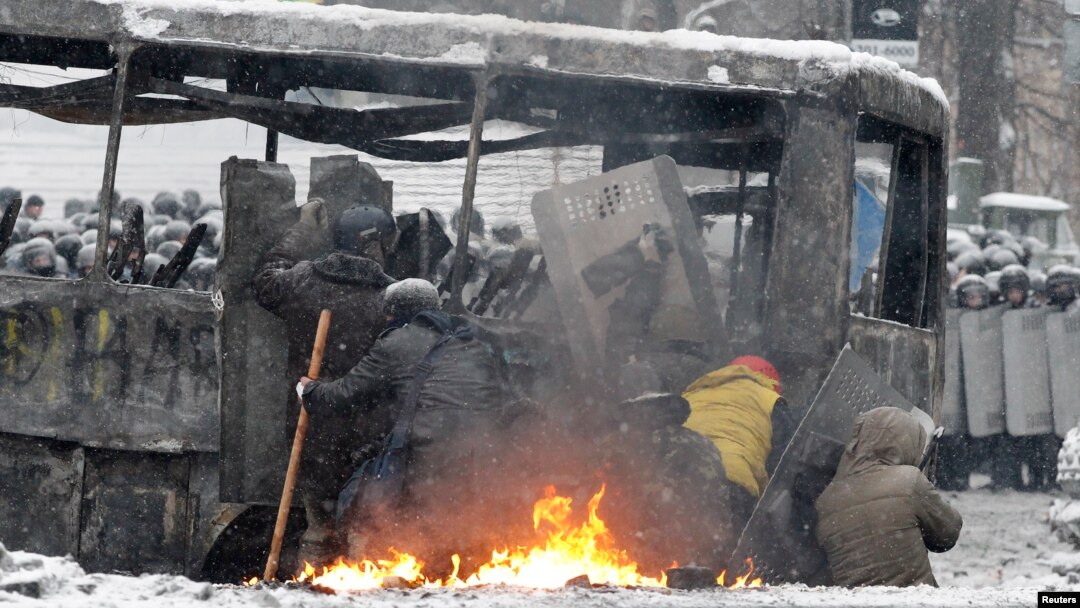 Pro-European protesters take cover behind a burnt bus during clashes with riot police in Kyiv, Jan. 22, 2014.