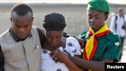 A woman is consoled by church members as she grieves near the graves of victims of a suicide bomb attack during a memorial service at St. Theresa's Church in Madalla, on the outskirts of Abuja, December 23, 2012. 