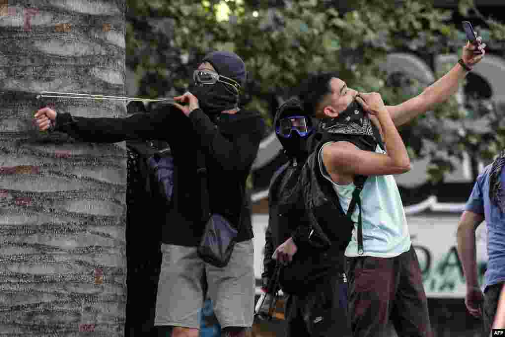 A demonstrator takes a selfie as another one uses a sling during a protest against the government's economic policies in Santiago, Chile, Nov. 6, 2019.